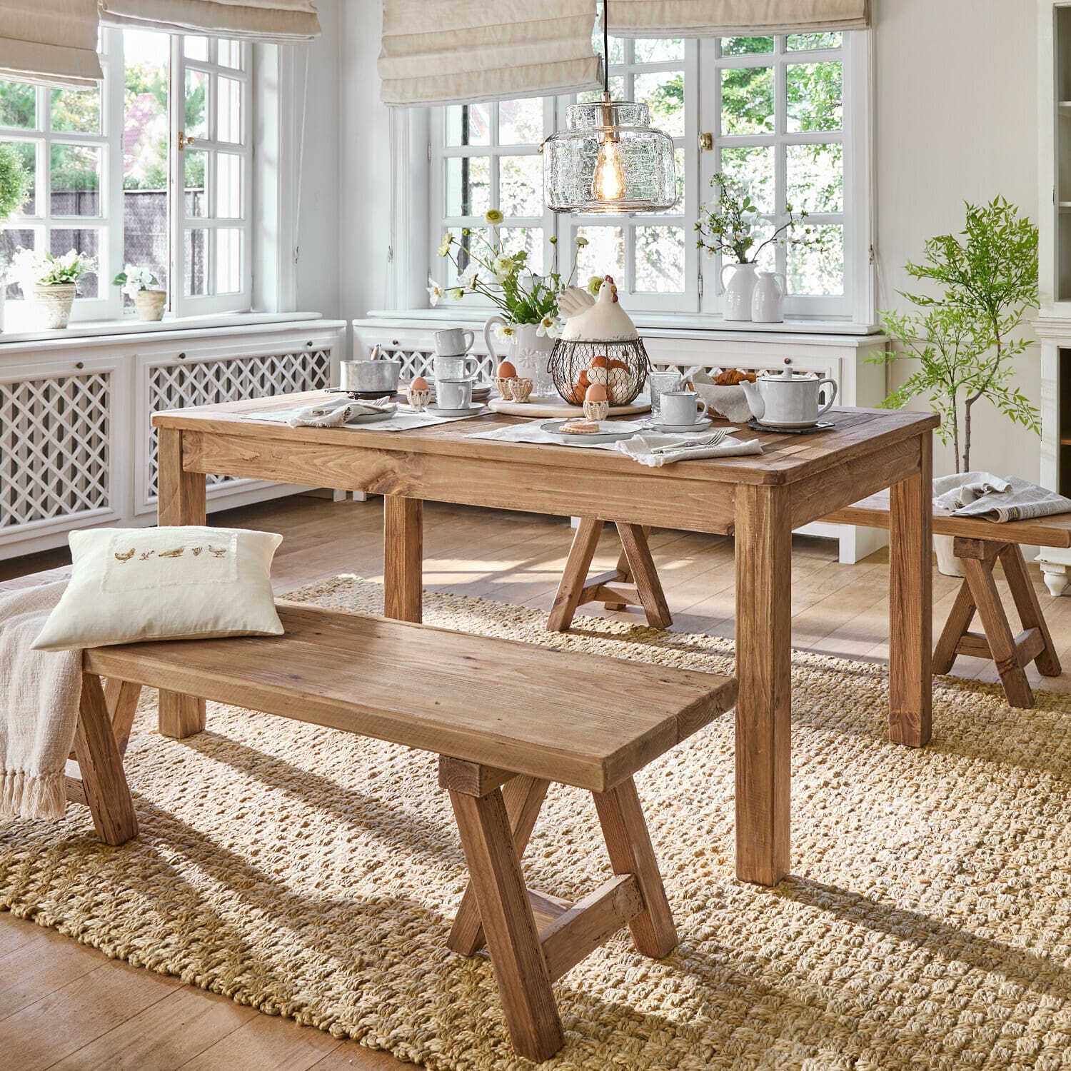 Tisch Amherst Esszimmer mit Holztisch und Bänken auf Naturteppich, helles Interieur mit Dekorationen und Licht