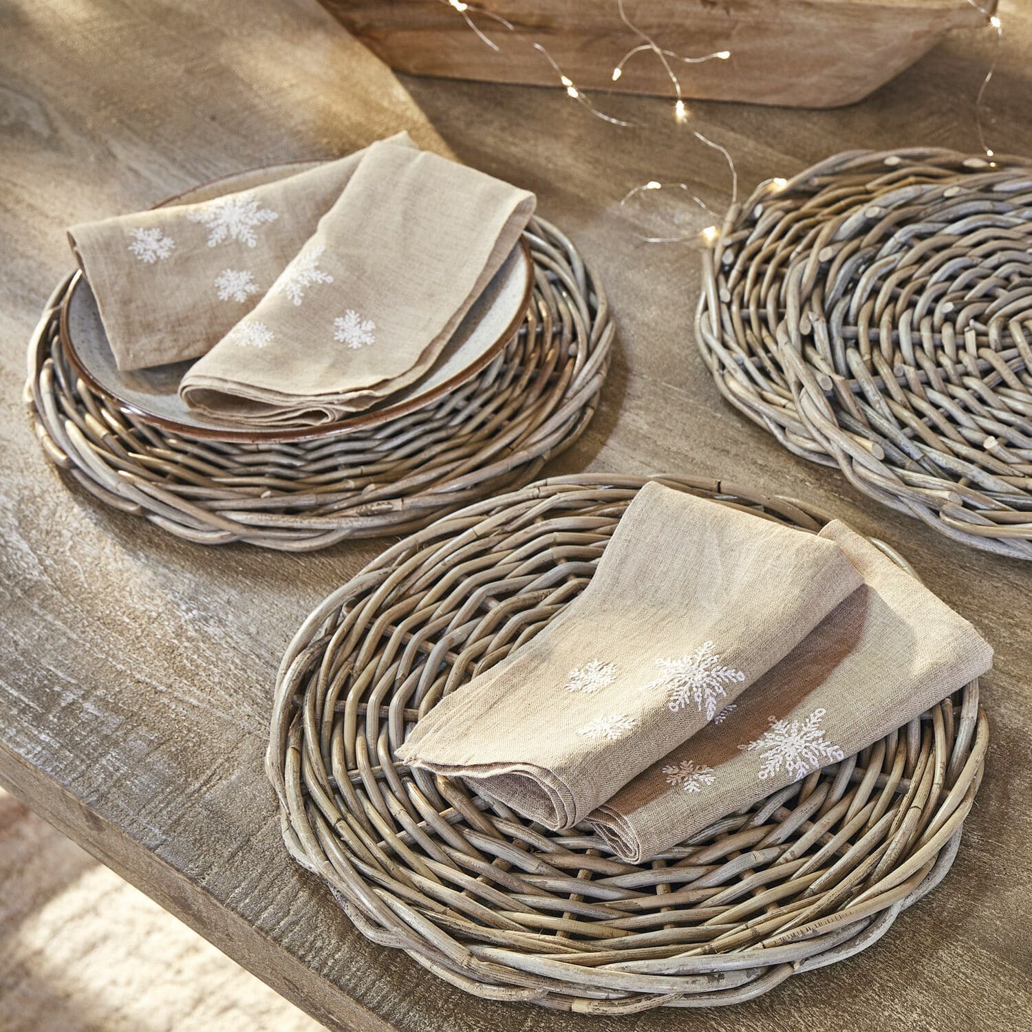Serviette 4er Set Ruspi Beige Leinenservietten mit Schneeflocken-Stickerei auf geflochtenen Weidenuntersetzern auf Holztisch