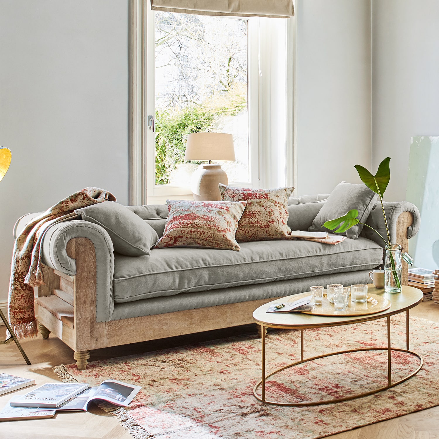 Graues Sofa mit Holzrahmen und dekorativen Kissen in hellem Wohnzimmer mit Fenster