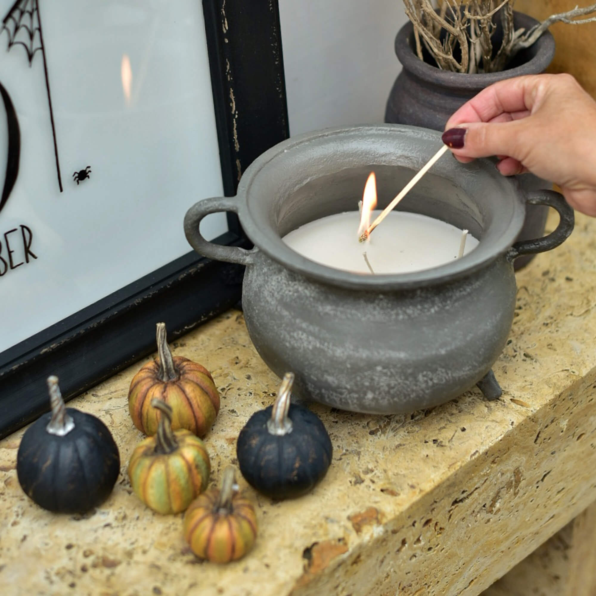 Graue Keramikkerze in Kesselform mit weißem Wachs und dekorativen Mini-Kürbissen auf Steinablage