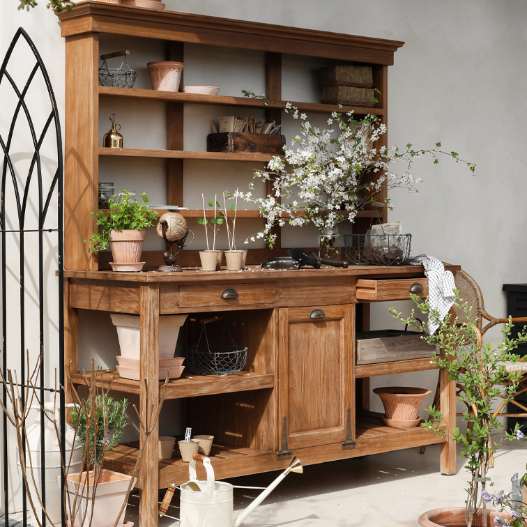 Holz-Gartenschrank mit Regalen, Blumentöpfen und blühenden Zweigen, dekoriert mit Gartengeräten