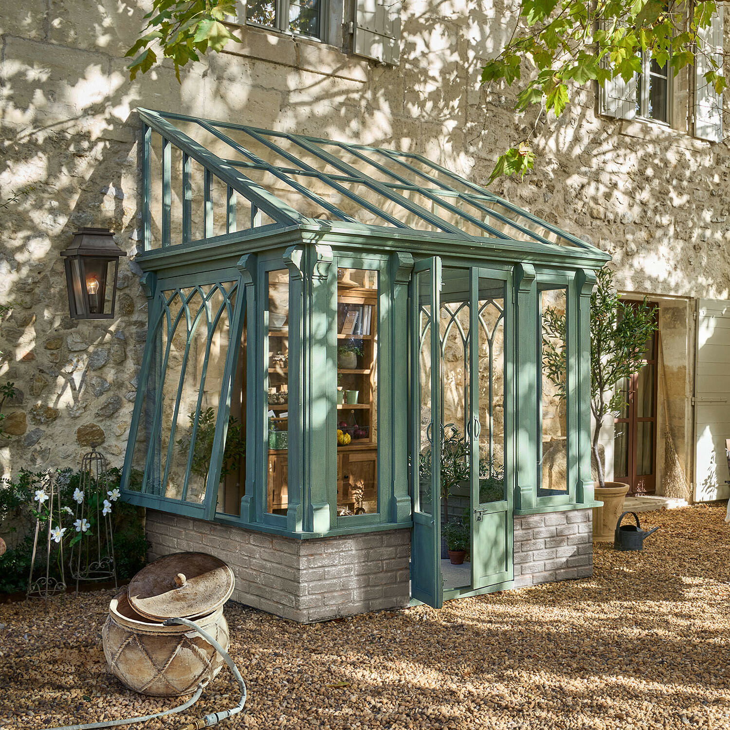 Grüne Holz-Gewächshaus mit Ziegelbasis auf Kiesboden in sonnigem Garten