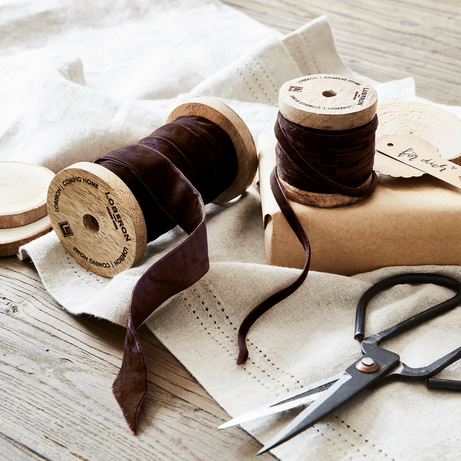 Braunes Samtband auf Holzspulen mit Schere auf Leinentuch, DIY-Dekoration und Bastelmaterial