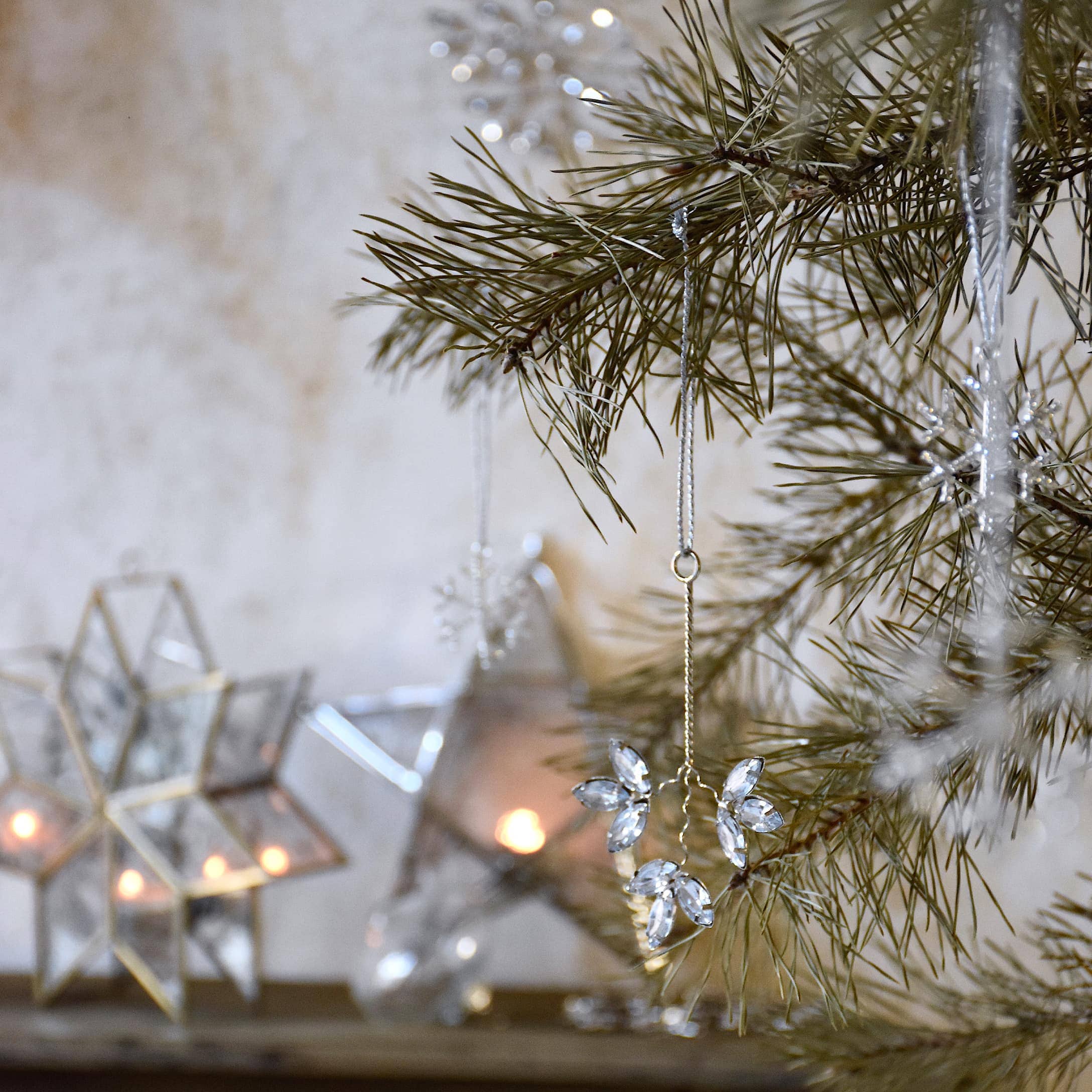 Weihnachtsdekoration mit Kristallanhängern an Kieferzweig und leuchtenden Sternen im Hintergrund