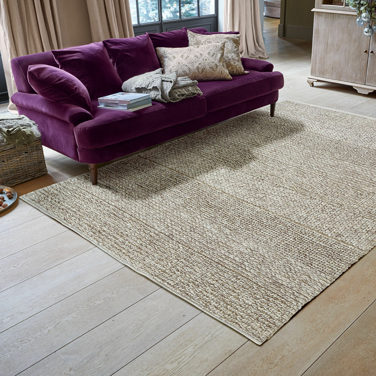 Teppich Welezas Beigefarbener Teppich aus Naturmaterial mit geflochtener Struktur im modernen Wohnzimmer mit violettem Sofa