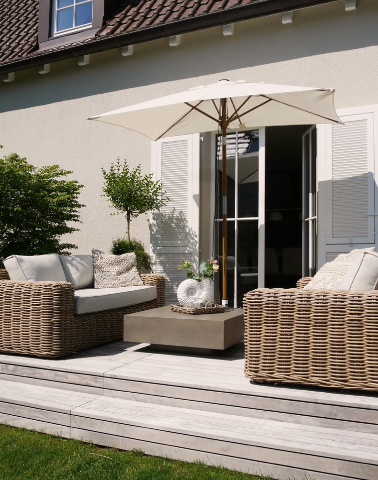 Moderner Gartenmöbel-Set aus beigem Rattan mit Sonnenschirm und Kissen auf hellem Holzdeck