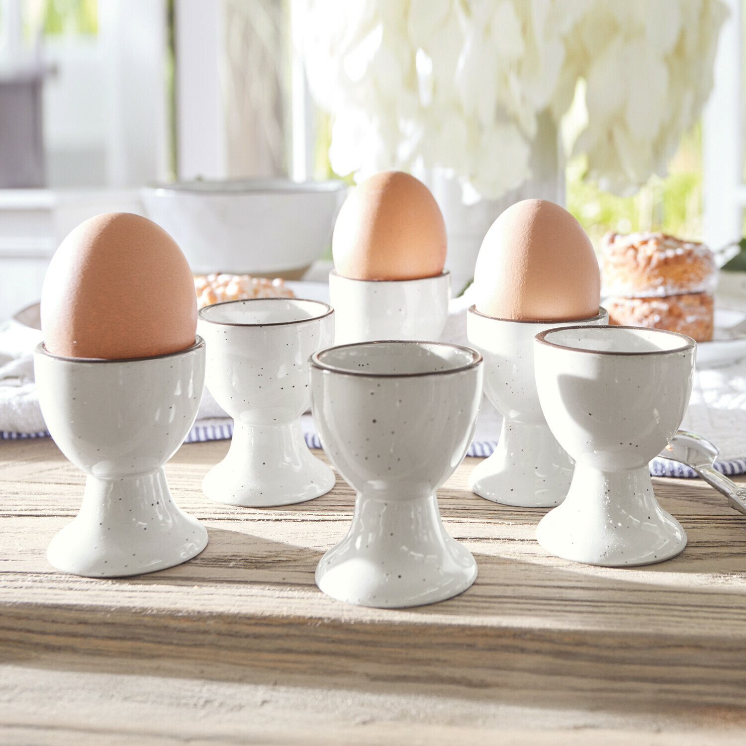 Eierbecher 6er Set Biarré Set aus weißen Keramik-Eierbechern mit braunen Eiern auf hellem Holztisch