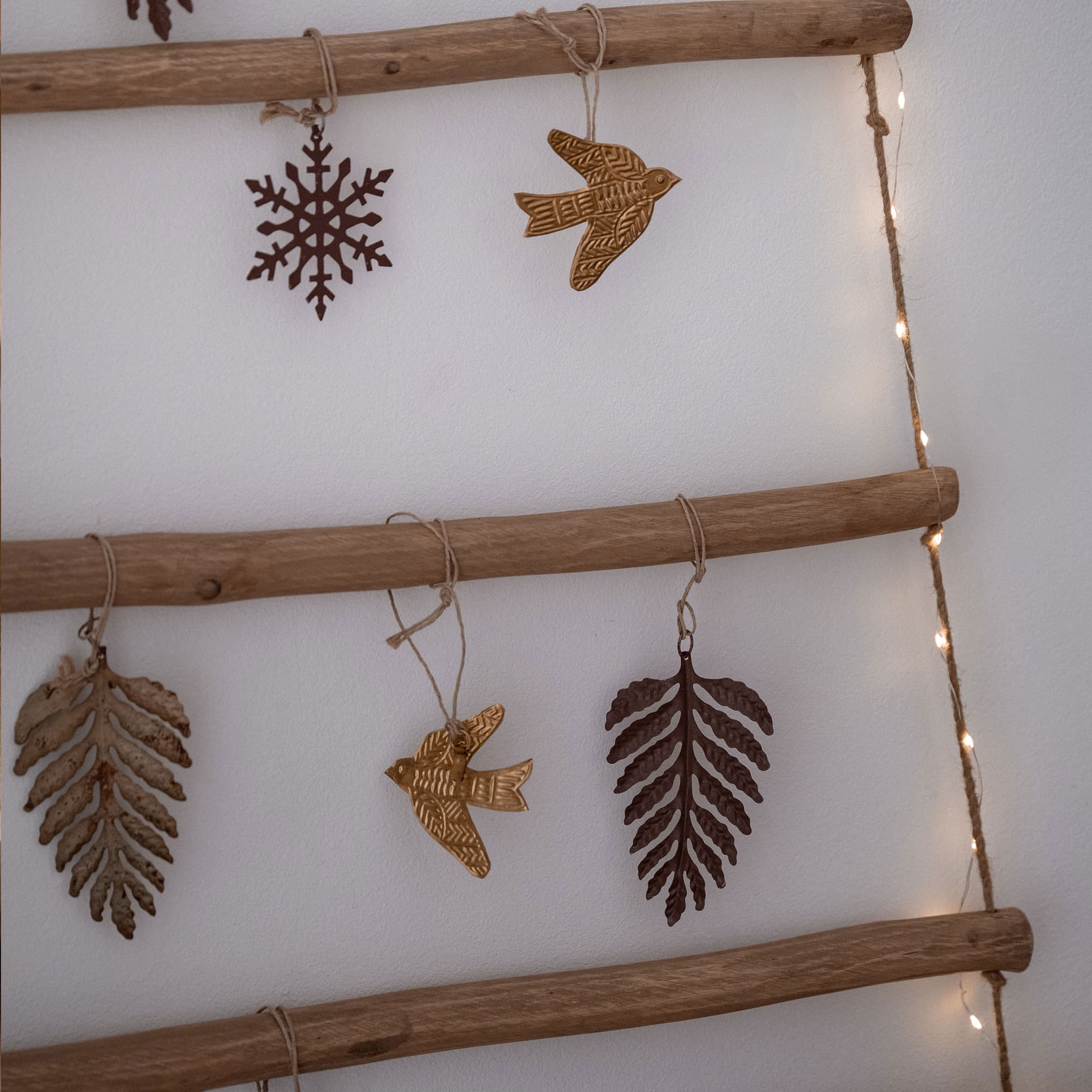 Metall-Weihnachtsschmuck in Form von Blättern, Vögeln und Schneeflocke an Holzleiter hängend