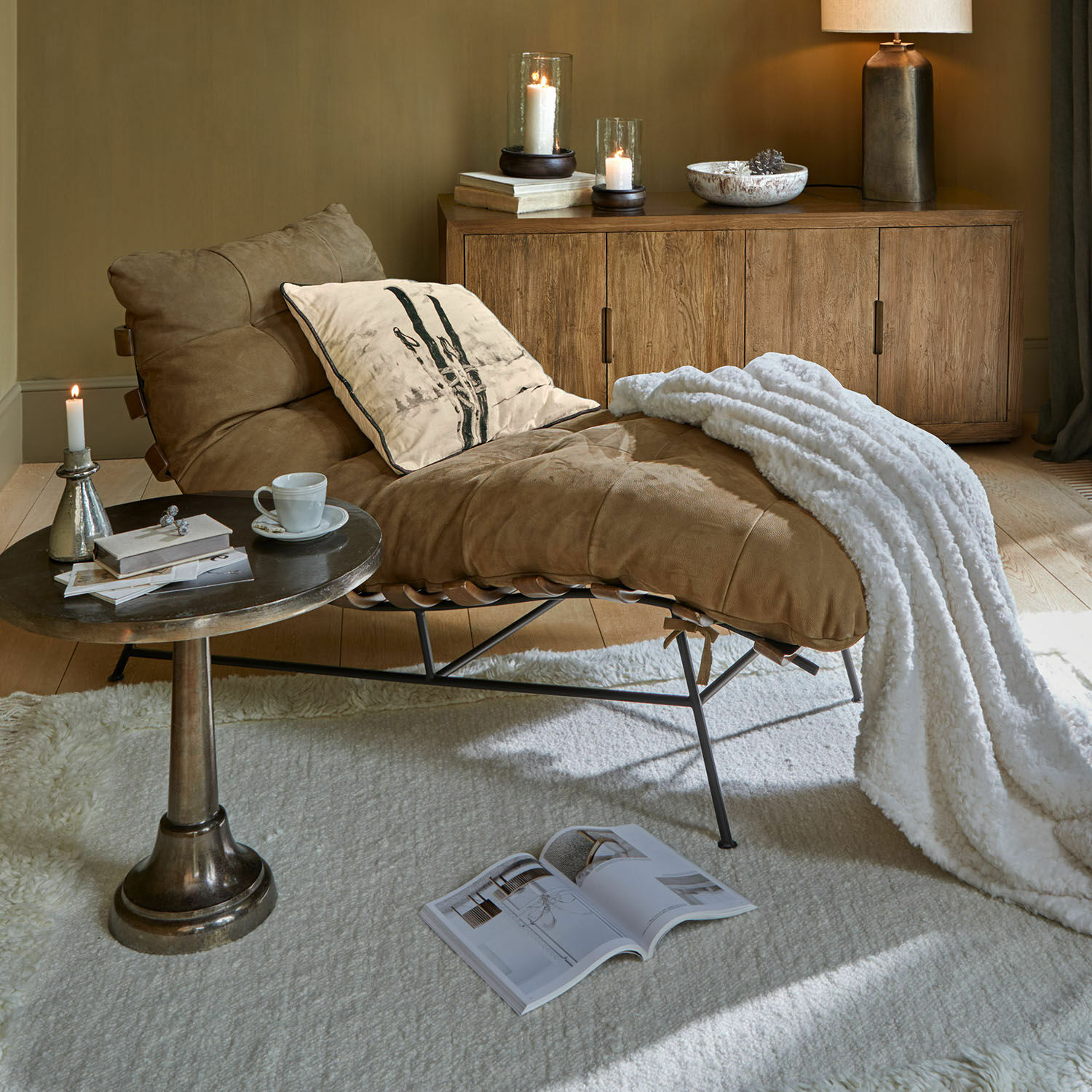 Chaiselongue Horraine Brauner Ledersessel mit weißer Decke und Kissen neben Holzkommode und Beistelltisch im Wohnzimmer