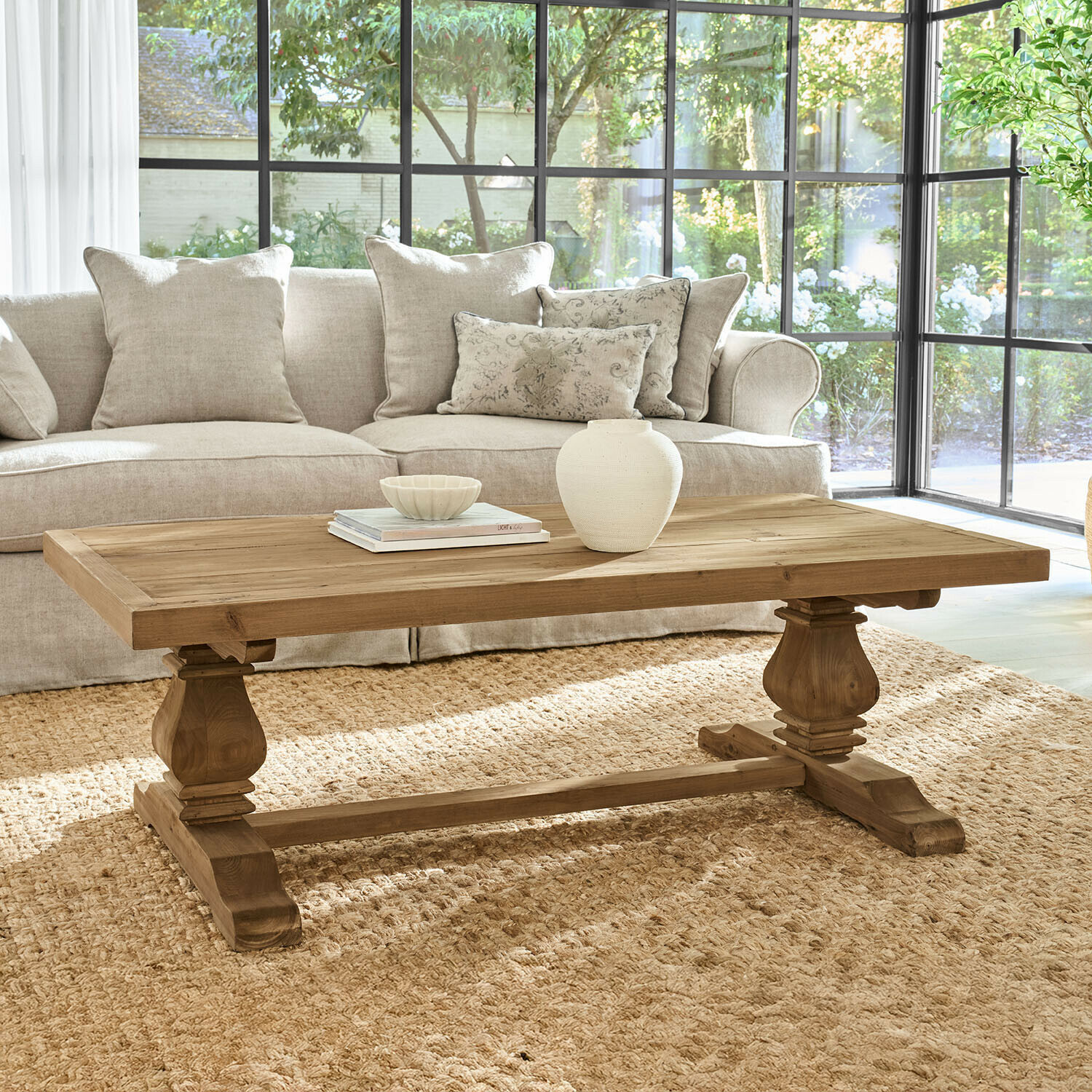 Holz-Couchtisch in Naturfarbe mit verzierten Beinen im hellen Wohnzimmer mit beigem Sofa