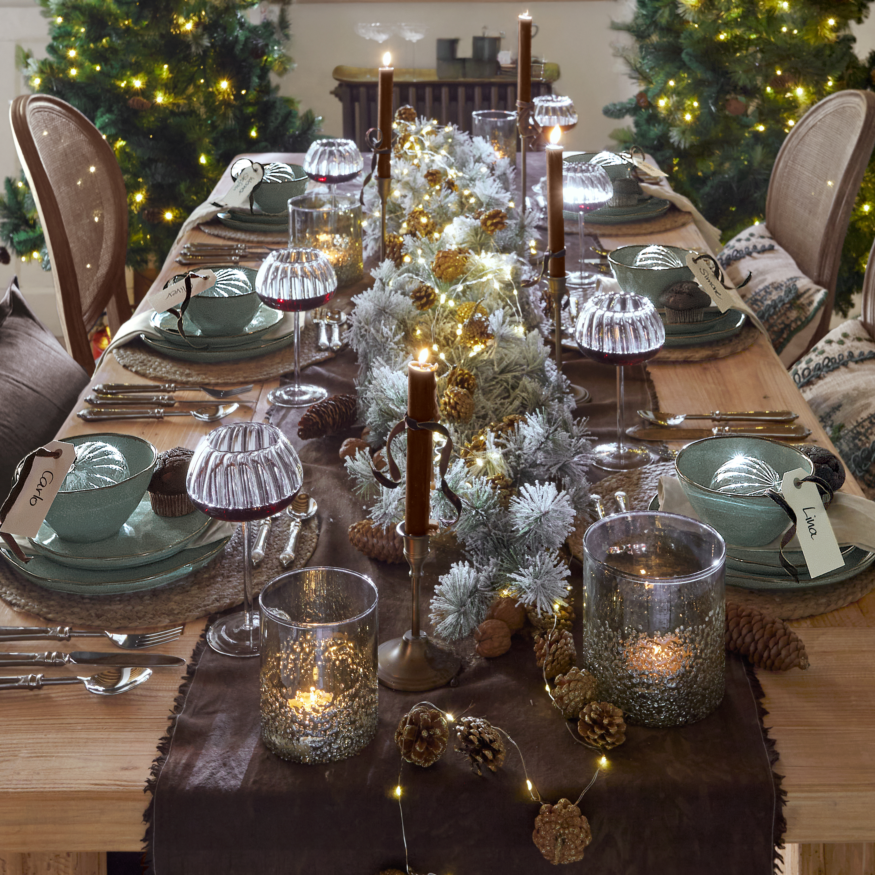 Weihnachtlich gedeckter Holztisch mit grüner Keramik, brennenden Kerzen und LED-Lichterkette als Dekoration