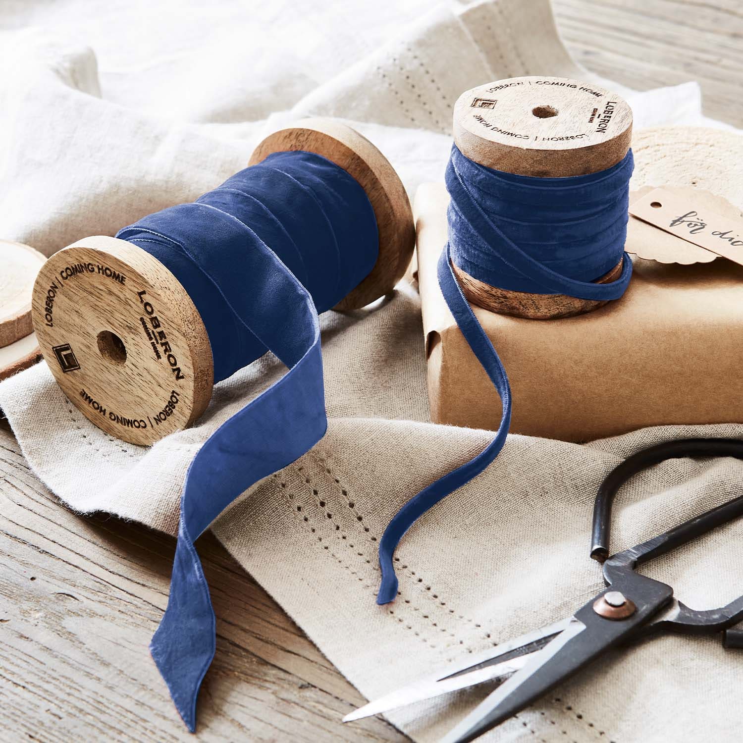Blaue Samtbänder auf Holzspulen mit Schere auf Leinenstoff für Dekoration und Basteln