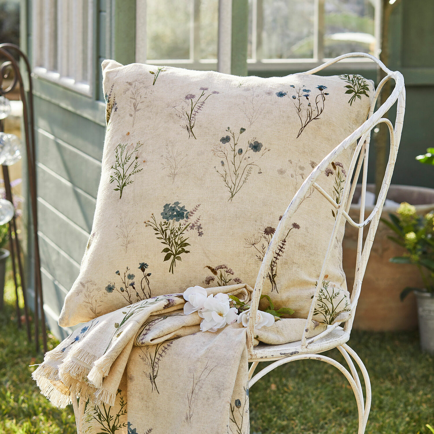 Kissenhülle Cabinda Beige Leinenkissen und Decke mit zartem Blumenmuster auf Metallstuhl im Garten