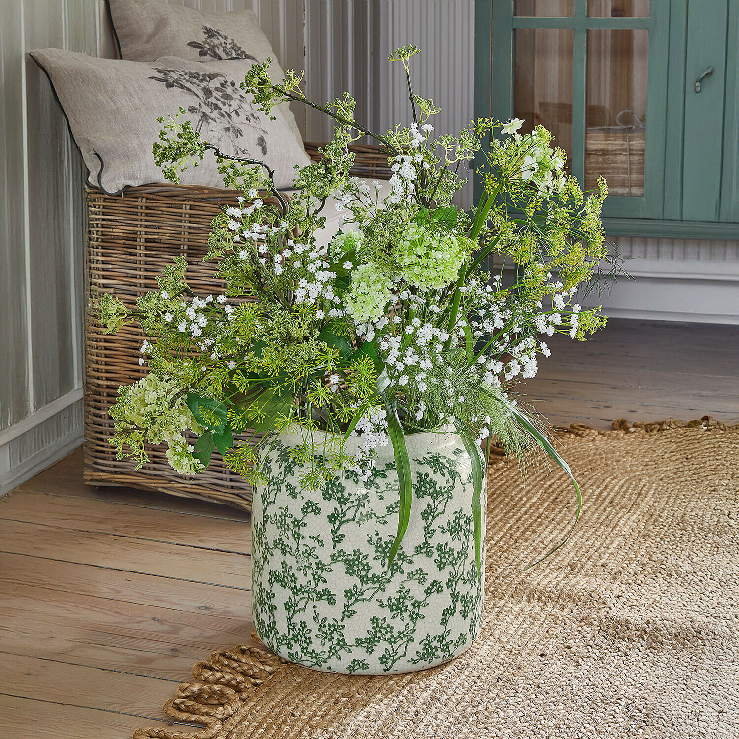 Weiße Keramikvase mit grünem Muster, gefüllt mit weißen und grünen Blumen auf Holzboden