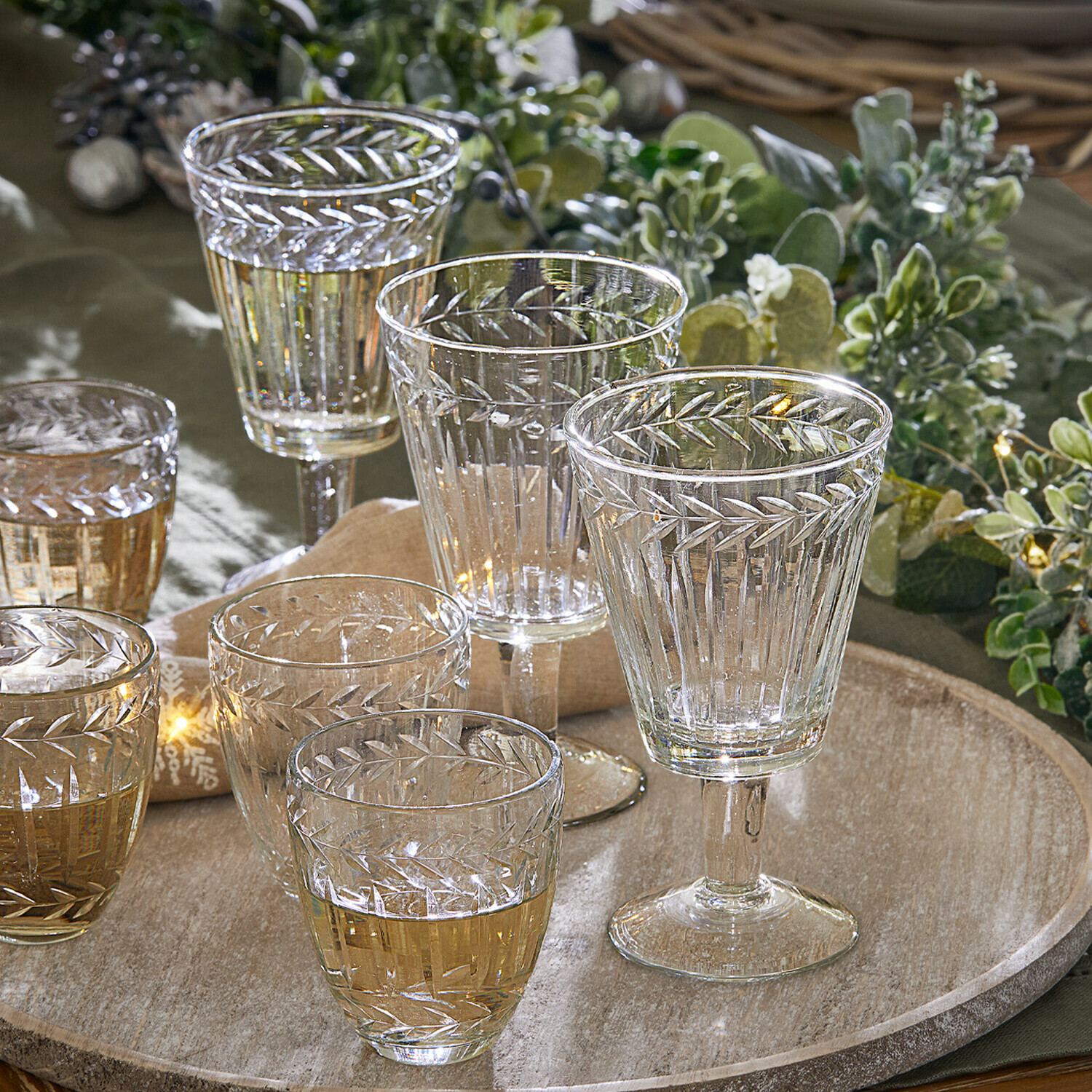 Set aus klaren Gläsern und Weingläsern mit graviertem Blattmuster auf einem Holztablett