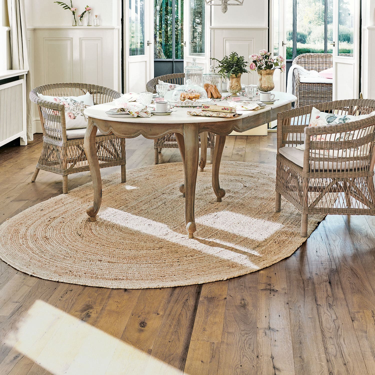 Teppich Ausone Heller Holztisch mit weißer Tischplatte auf rundem Jute-Teppich in hellem Raum mit Rattanstühlen