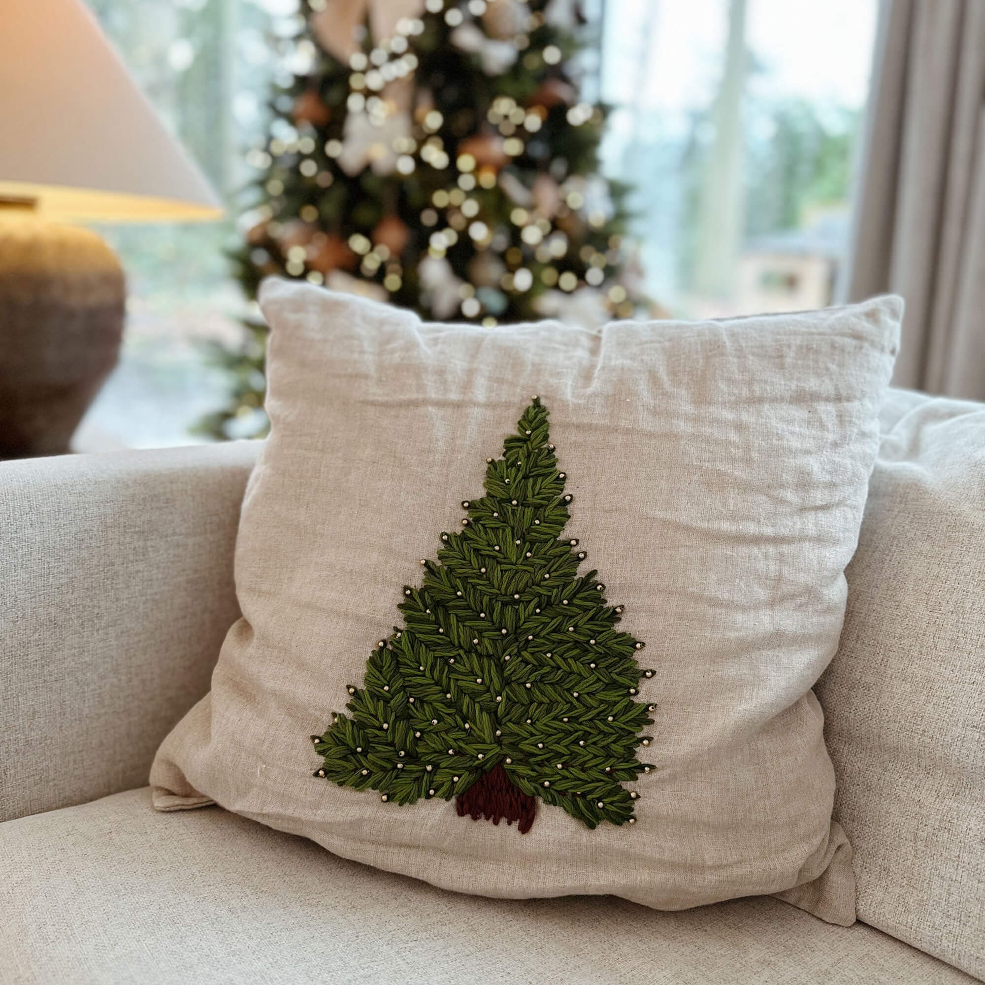Beige Leinenkissen mit grünem Tannenbaum-Stickmuster und braunem Stamm auf Sofa im Wohnzimmer