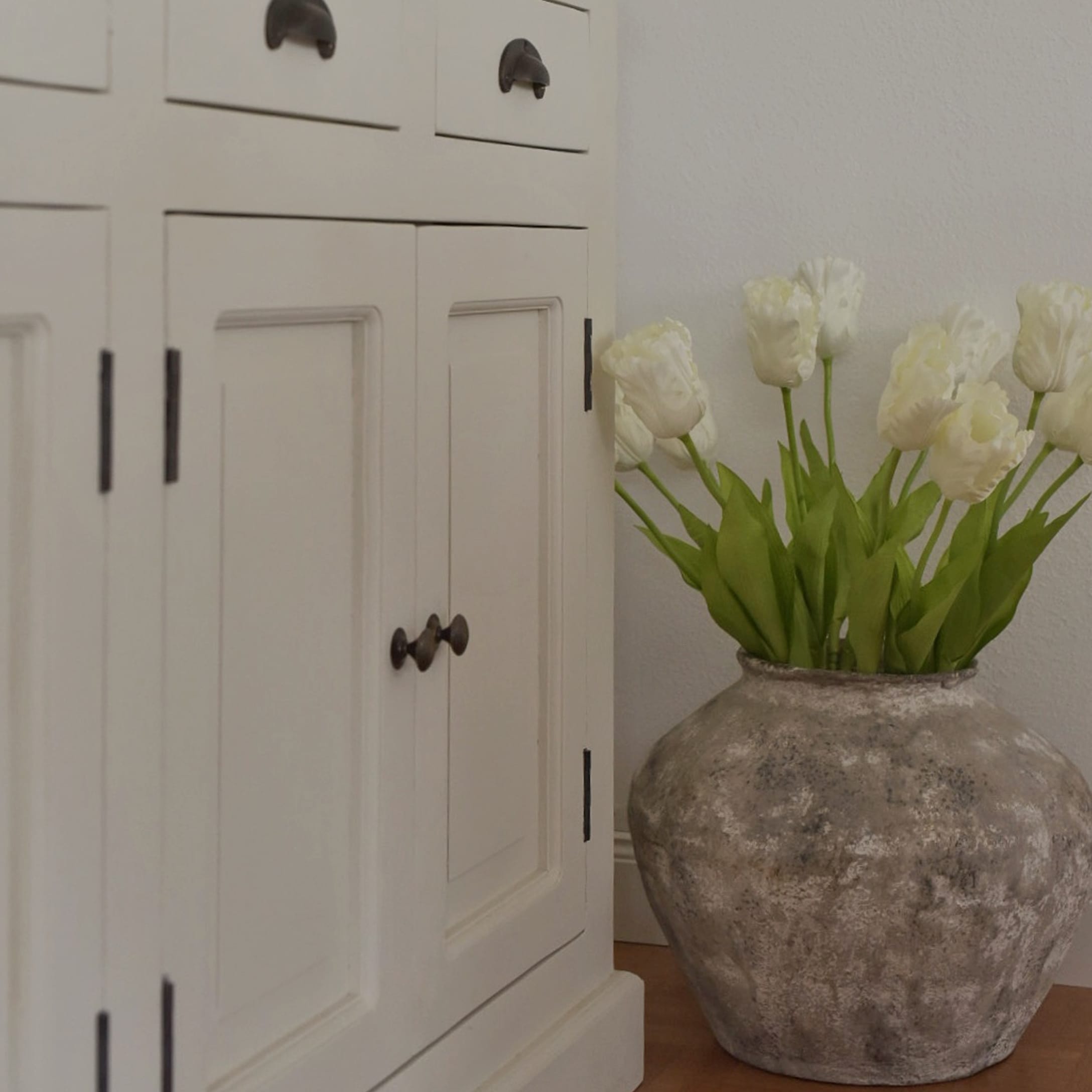 Große graue Keramikvase mit weißen Tulpen neben einem weißen Holzschrank