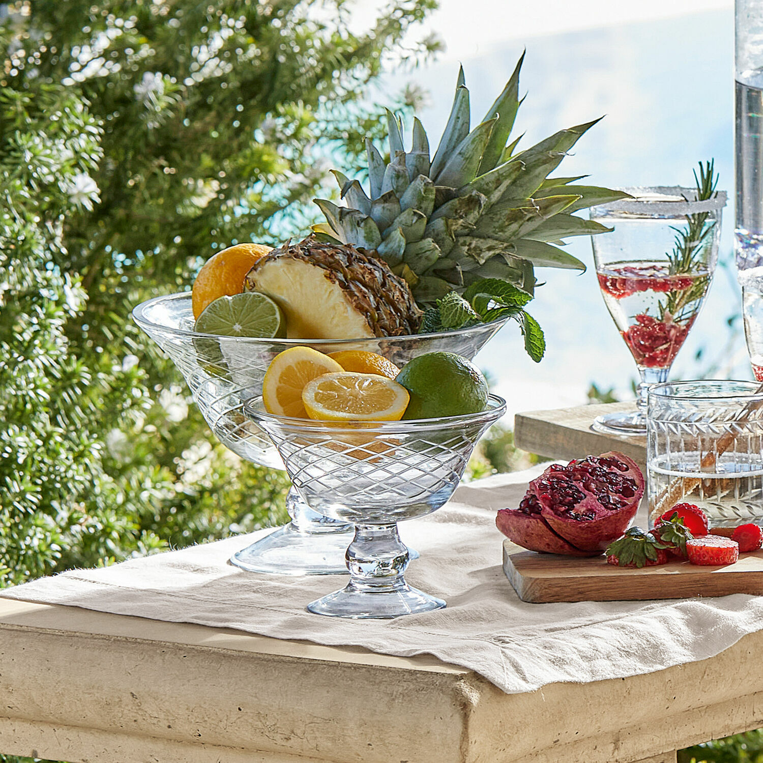 Schalen 2er Set Kadence Glas-Schalen auf Fuß mit Zitrusfrüchten und Ananas auf hellem Tisch im Freien
