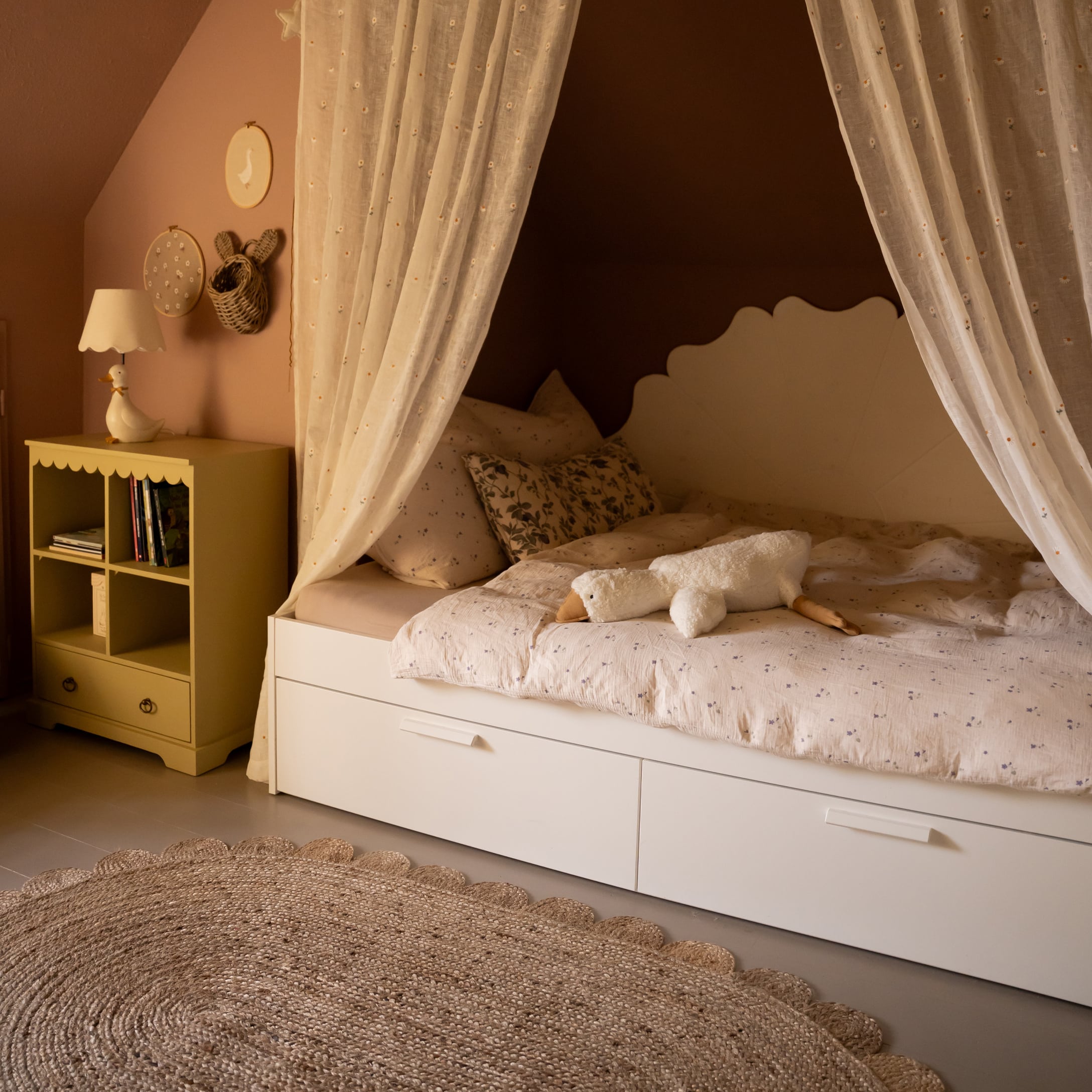 Gemütliches Kinderbett mit weißem Rahmen, Vorhängen und Plüschgans auf gemusterter Bettdecke