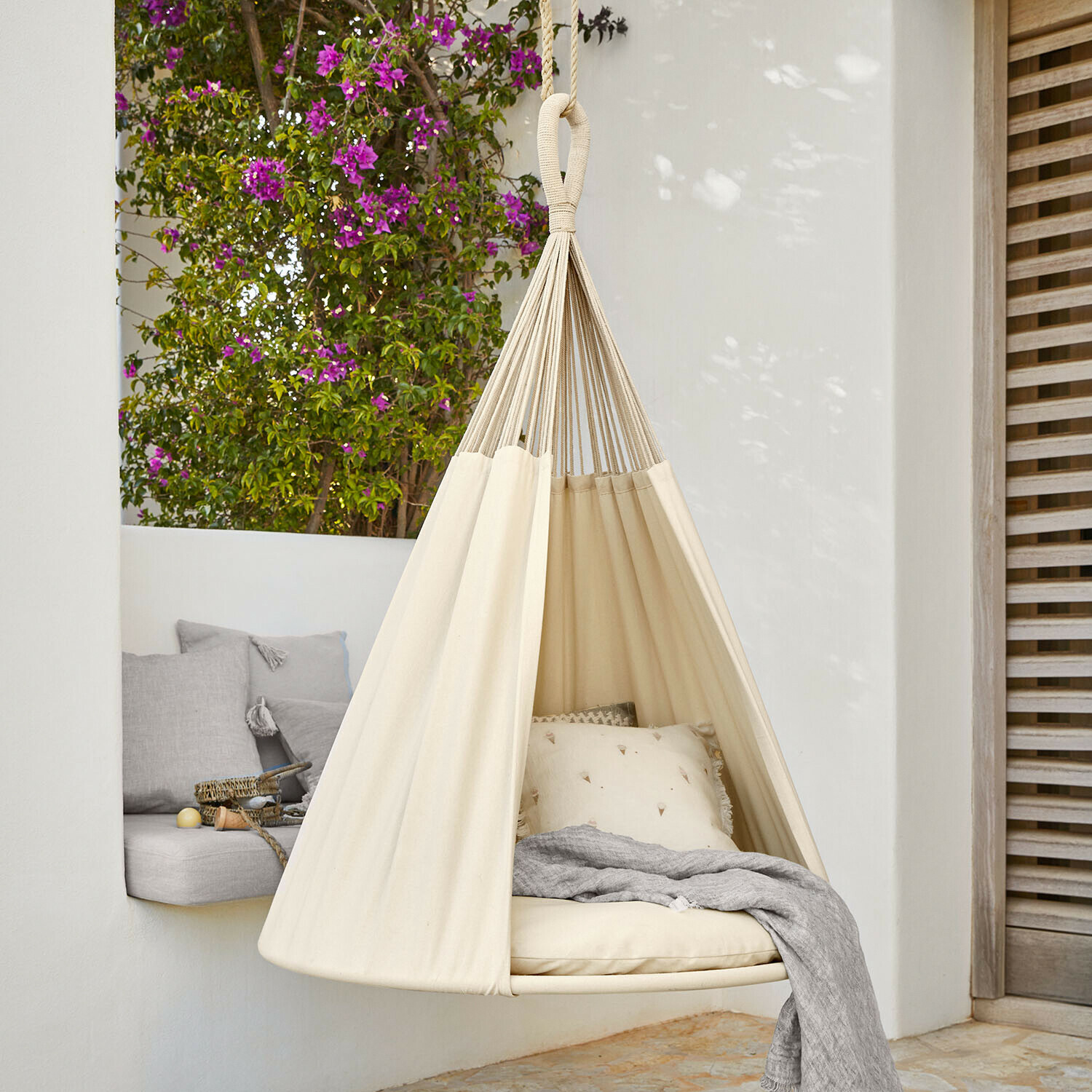 Beiger Baumwoll-Hängesessel mit Kissen und grauer Decke auf Terrasse mit Blumen