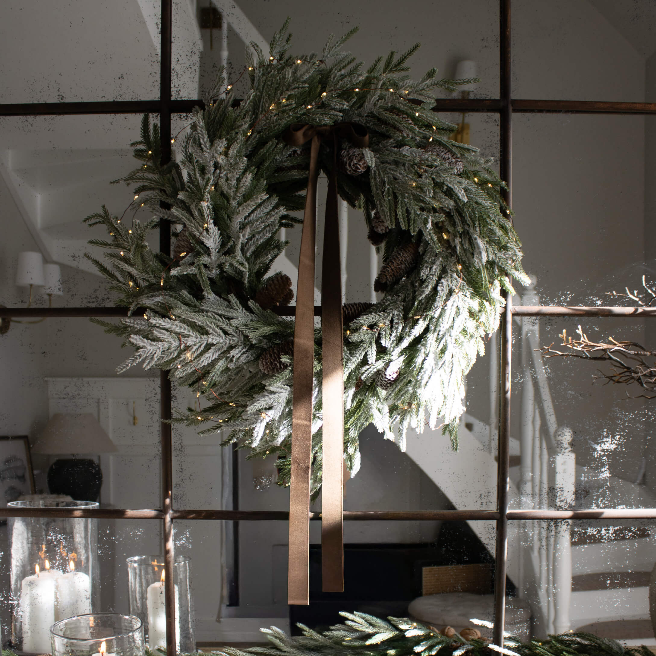 Weihnachtlicher Kranz aus grünen Zweigen mit Zapfen und braunem Band an Spiegel, festliche Dekoration