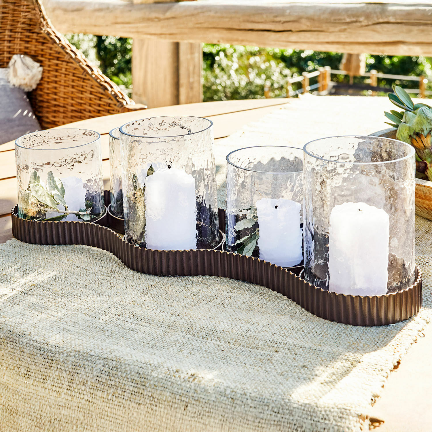 Windlicht Méridienn Set aus 5 Glaswindlichtern mit weißen Kerzen auf braunem Metallständer auf Gartentisch