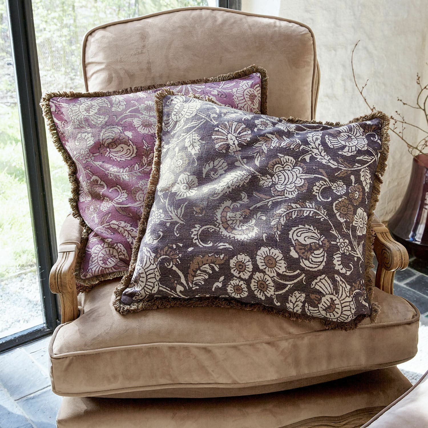 Kissenhülle 2er Set Lalluga Zwei dekorative Kissen mit floralem Muster in Violett und Grau auf einem beigen Sessel