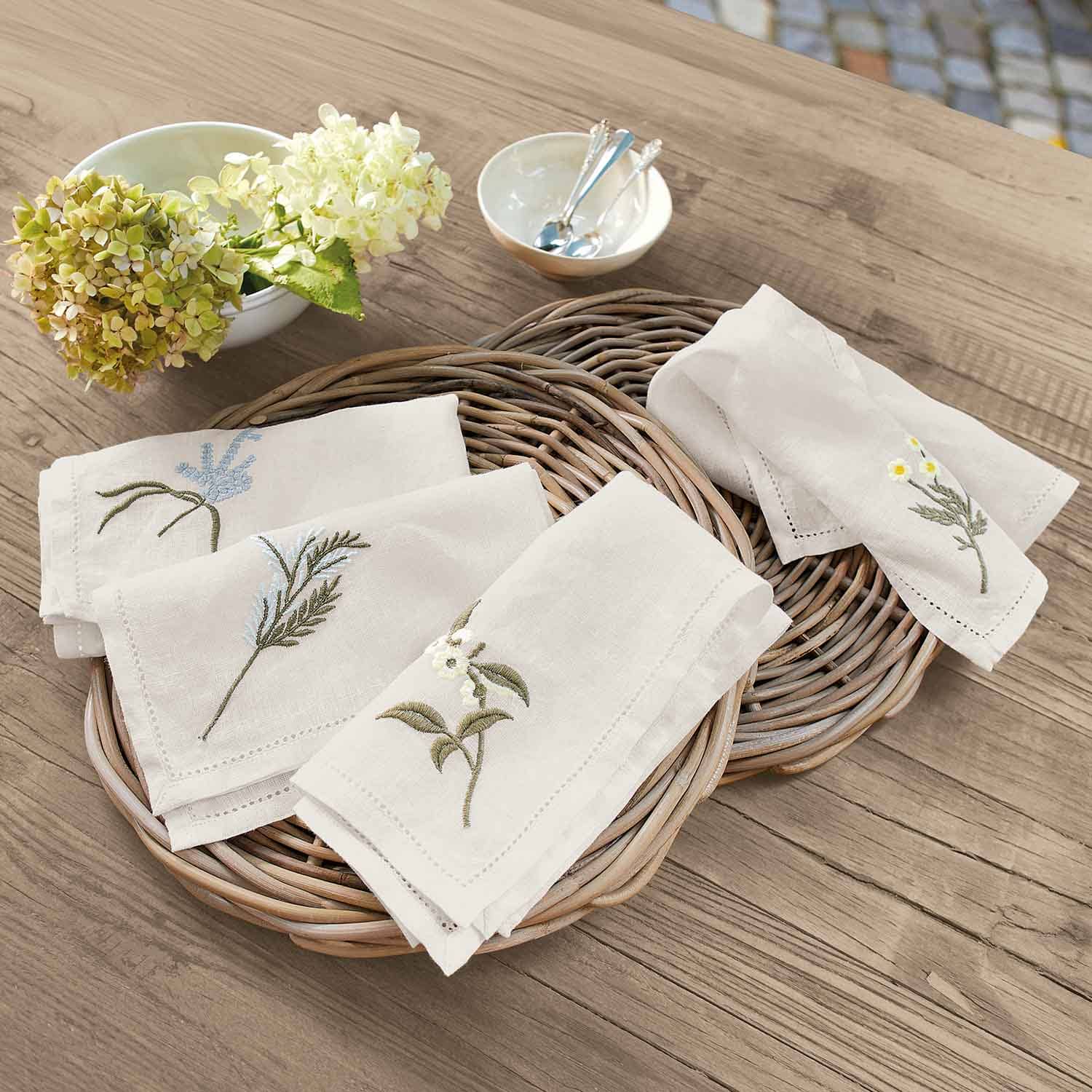 Leinenservietten in Creme mit bestickten Blumen auf einem Weidenkorb auf Holztisch