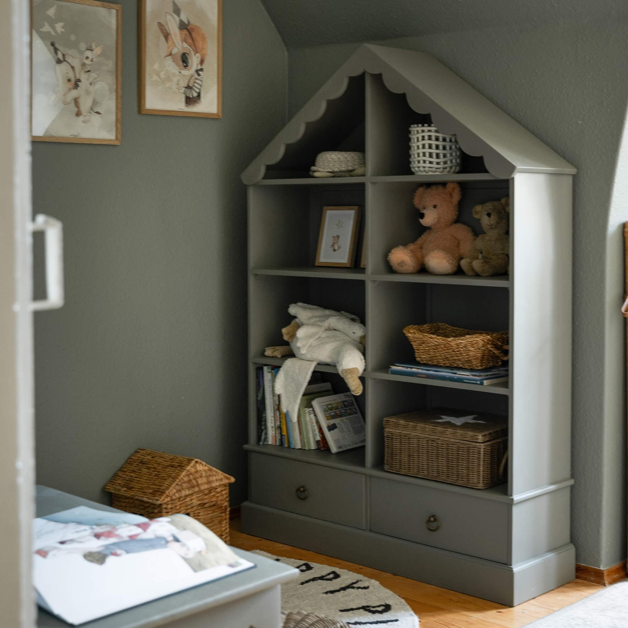 Graues Holzregal in Hausform mit Kuscheltieren und Körben im Kinderzimmer
