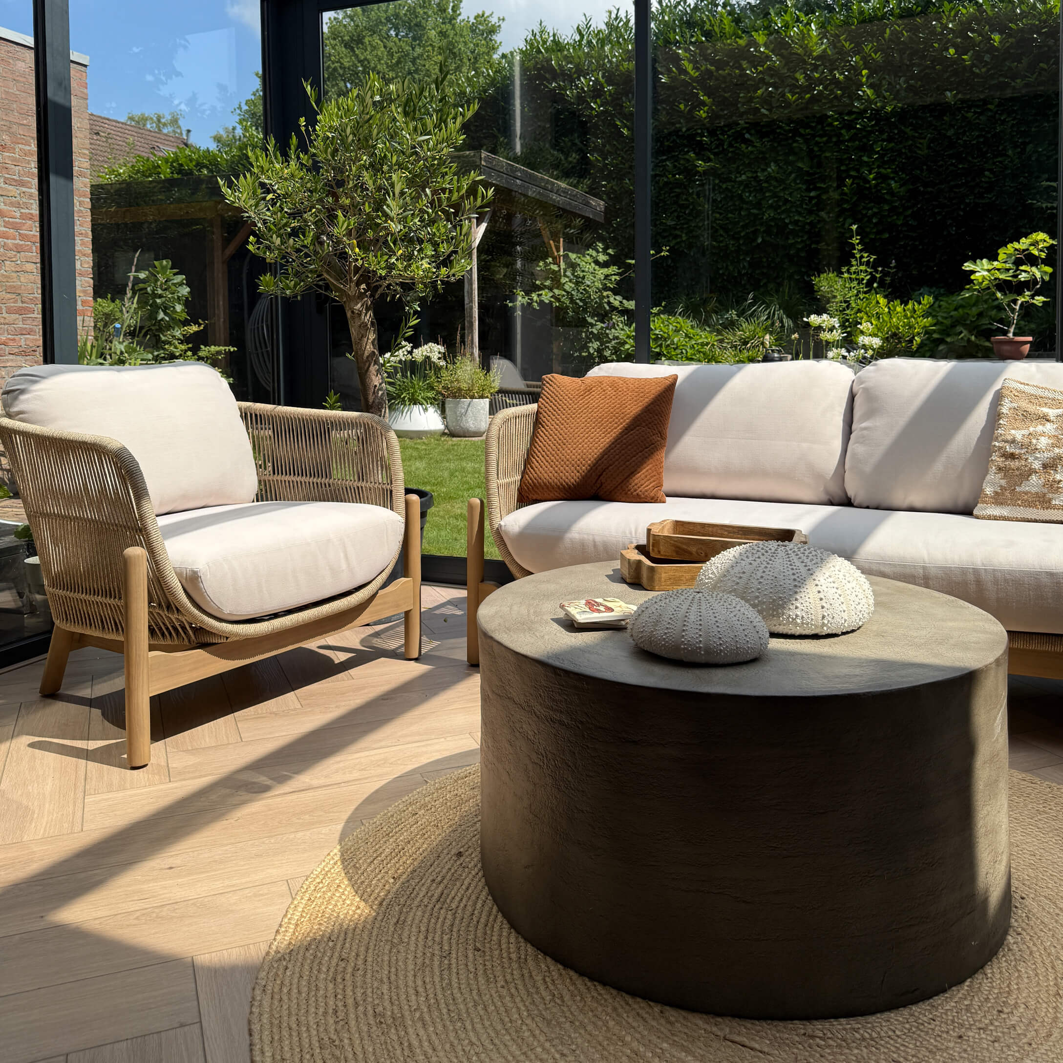 Moderner Wohnbereich mit beigem Sofa, Holz- und Stoffsessel sowie rundem schwarzem Couchtisch