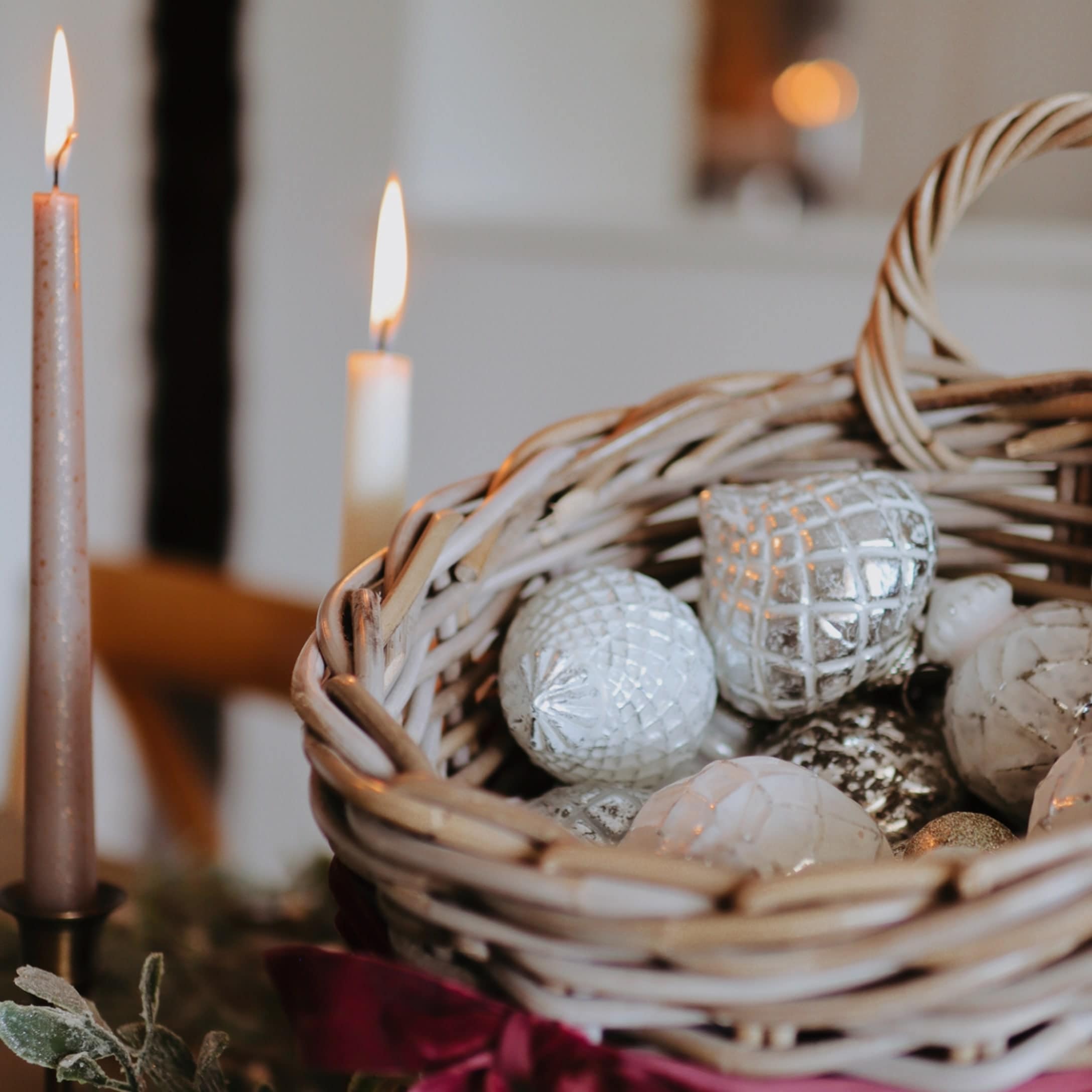 Wikingerkorb mit weißen und silbernen Weihnachtskugeln und zwei brennenden Kerzen