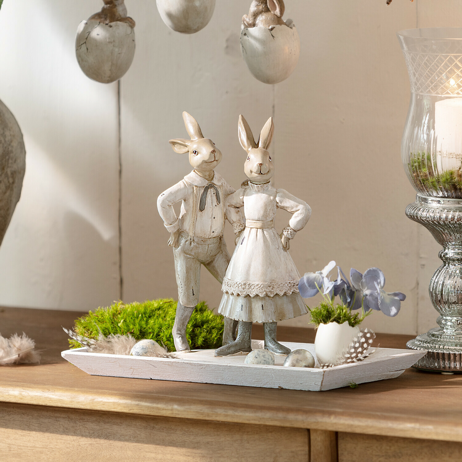 Dekoration mit zwei weißen Holzhasen auf Holztablett mit grünem Moos und dekorativen Eiern
