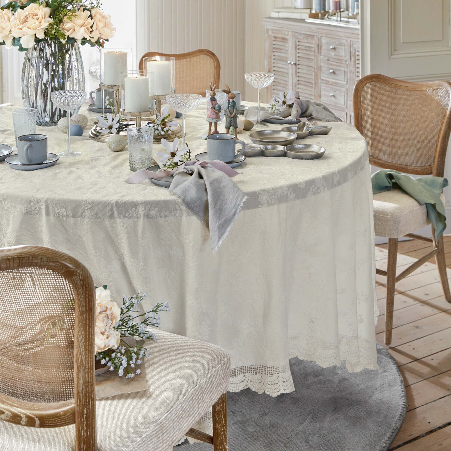 Eleganter Tisch mit cremefarbenem Spitzen-Tischdecke, Osterdekoration und grauem Geschirr
