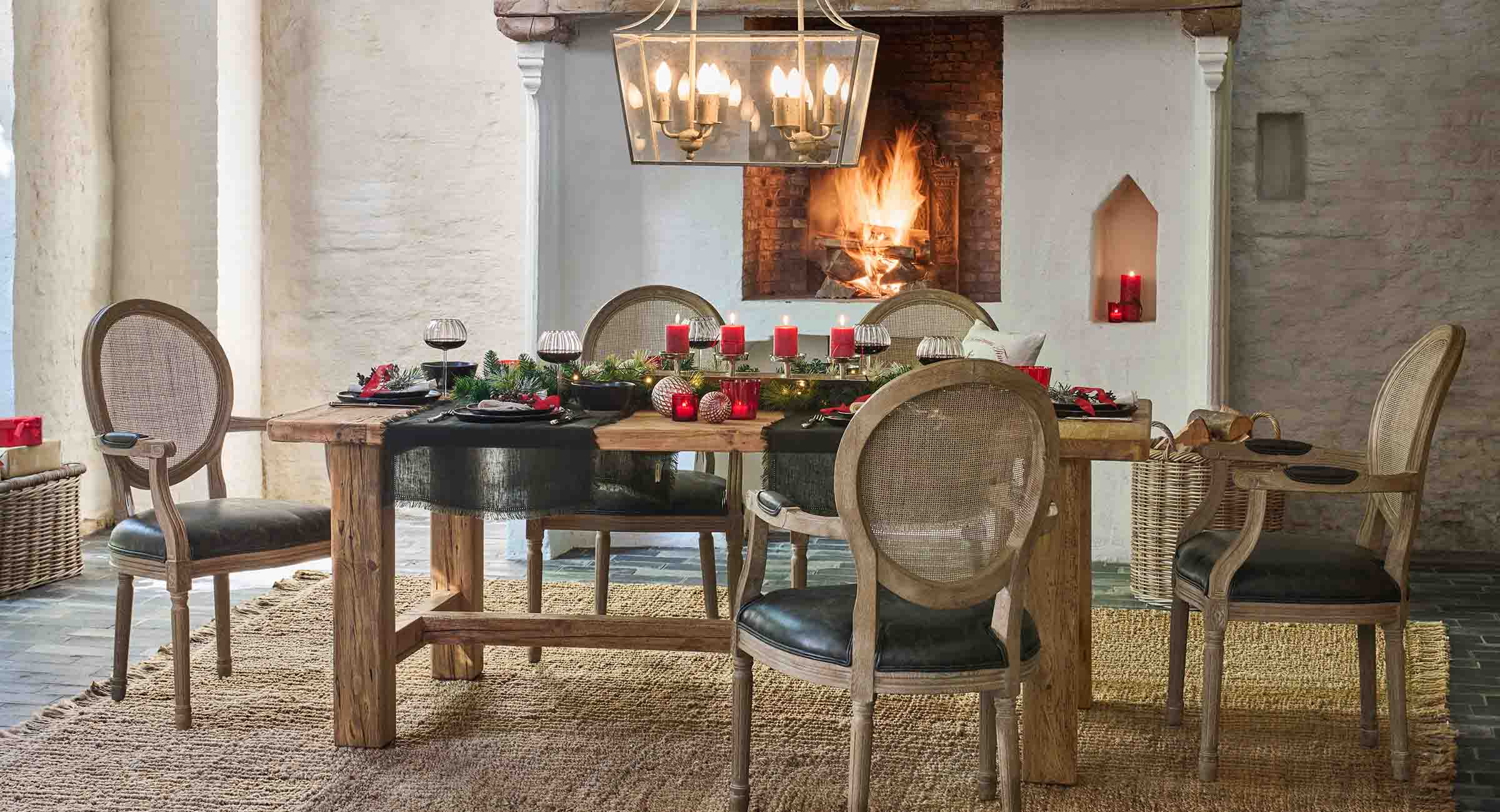 Rustikaler Holztisch mit natürlichen Dekorationen und roten Kerzen vor einem brennenden Kamin