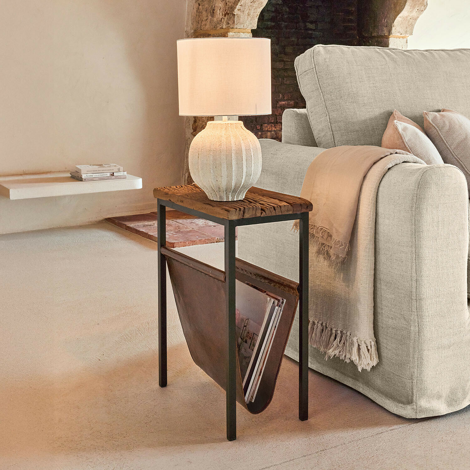 Beistelltisch mit Holzplatte und Lederfach für Zeitschriften neben beigem Sofa mit Tischlampe