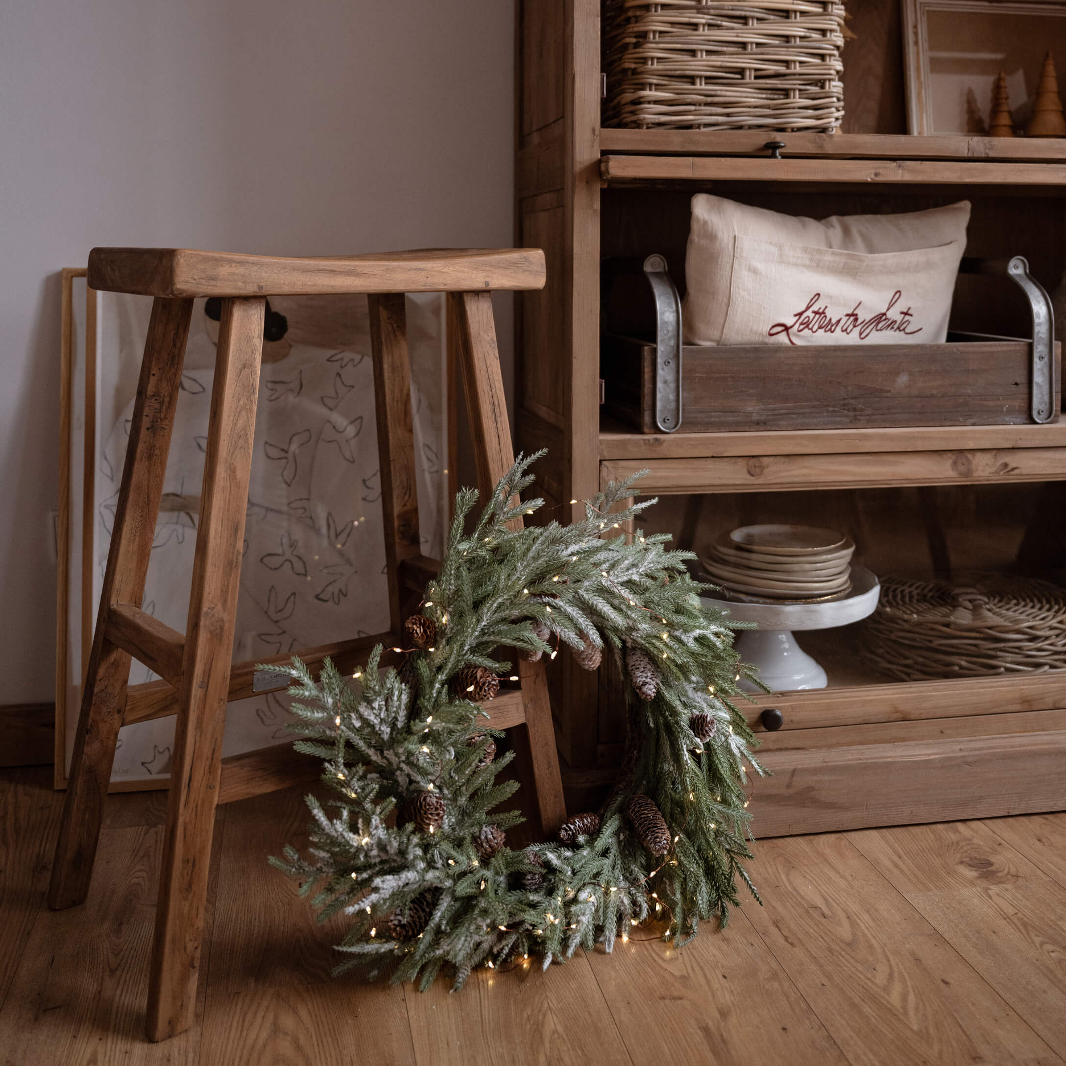Weihnachtlicher Dekokranz mit grünen Zweigen und Zapfen auf Holzboden neben einem Holzschemel