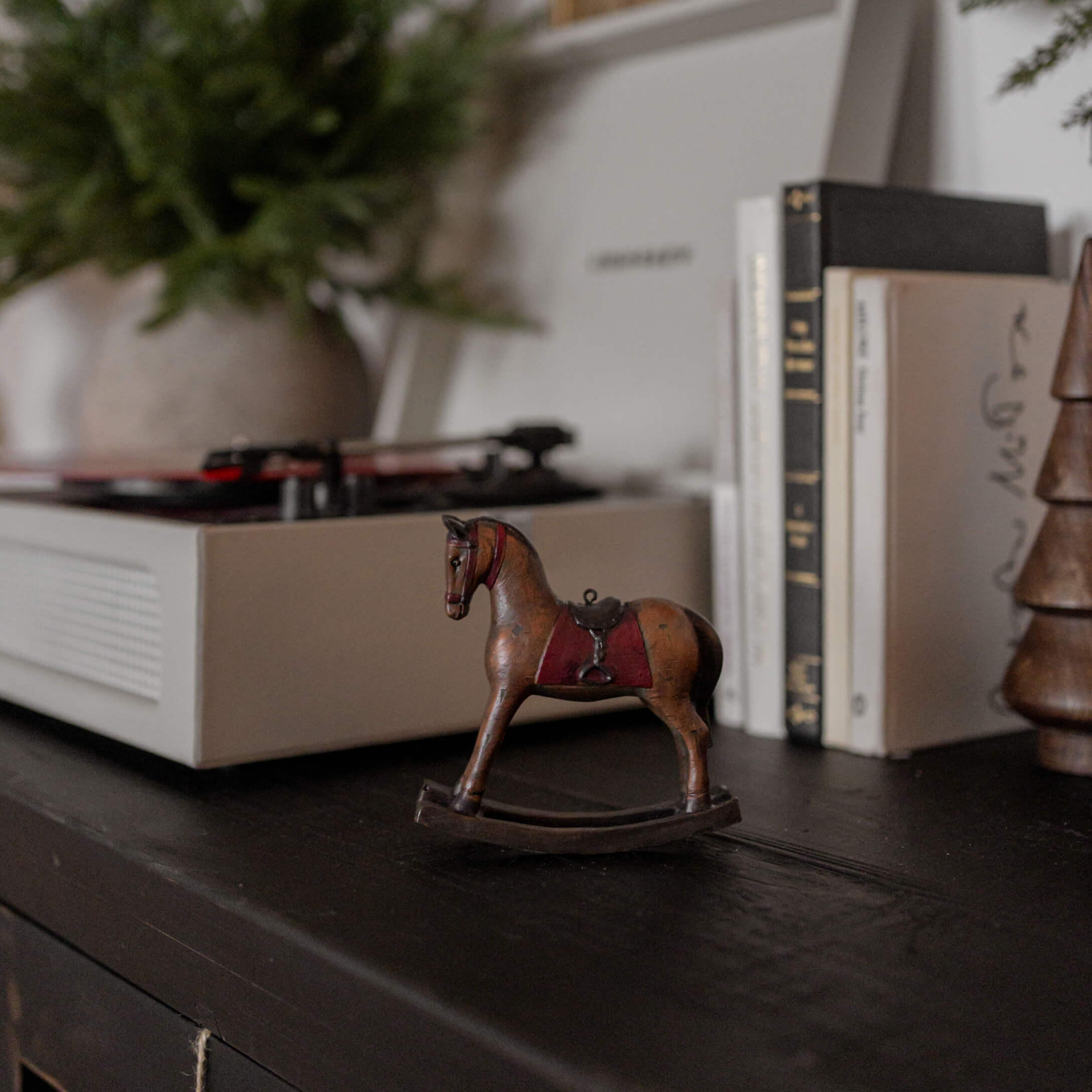 Braunes Holzschaukelpferd mit rotem Sattel auf schwarzer Oberfläche neben Büchern und Plattenspieler