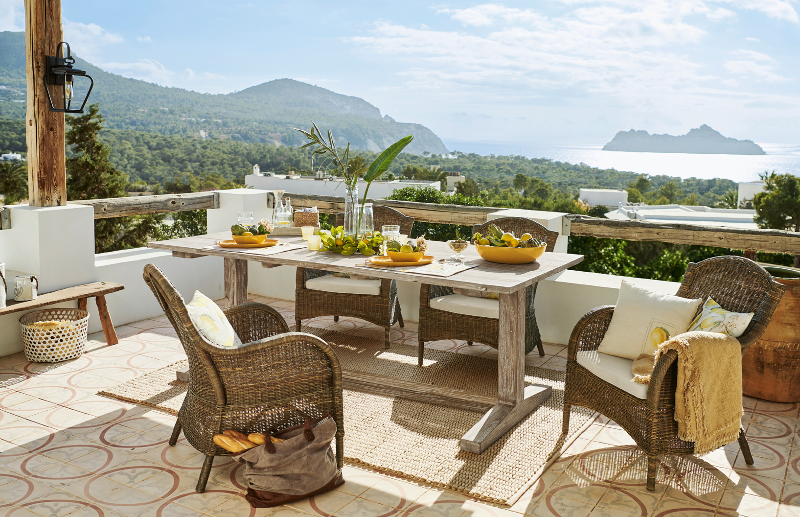 Terrasse mit Rattanmöbeln und hellem Holztisch mit Meer- und Bergblick im mediterranen Stil