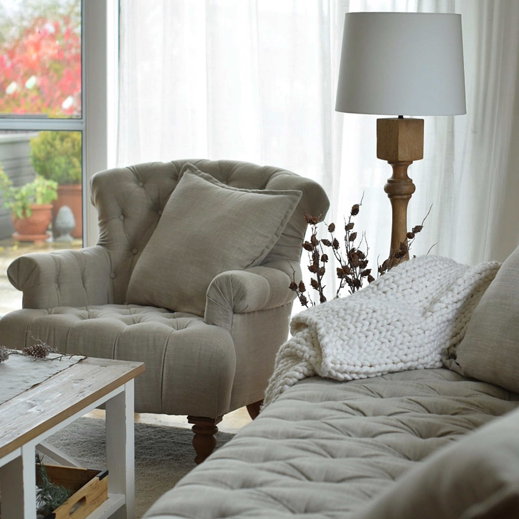 Beiger gepolsterter Sessel und Sofa mit Kissen und weißer Strickdecke in gemütlichem Wohnzimmer