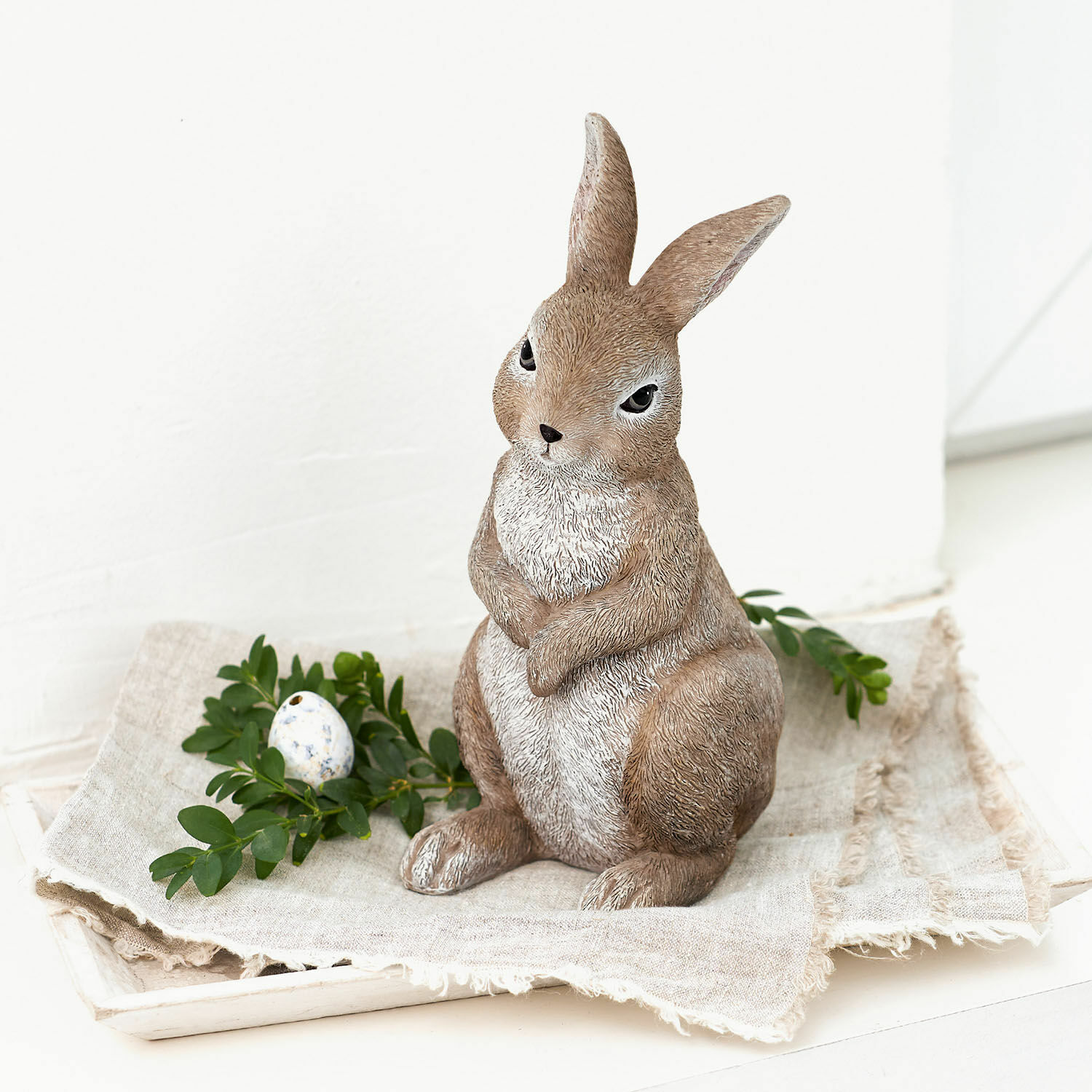 Deko-Hase Milli Dekorative braun-weiße Hasenfigur aus Kunststein auf Leinenstoff mit grünen Blättern und Ei