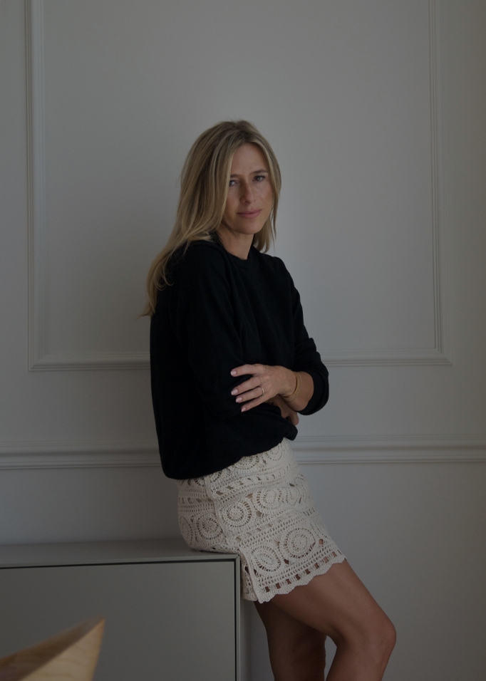 Frau in schwarzem Pullover und cremefarbener Spitzenrock vor hellem Wandhintergrund, Damenmode