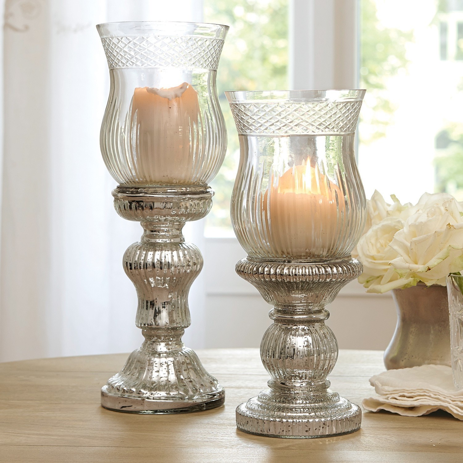 Zwei dekorative Kerzenhalter aus Glas mit antik-silbernem Effekt auf Holztisch in hellem Raum