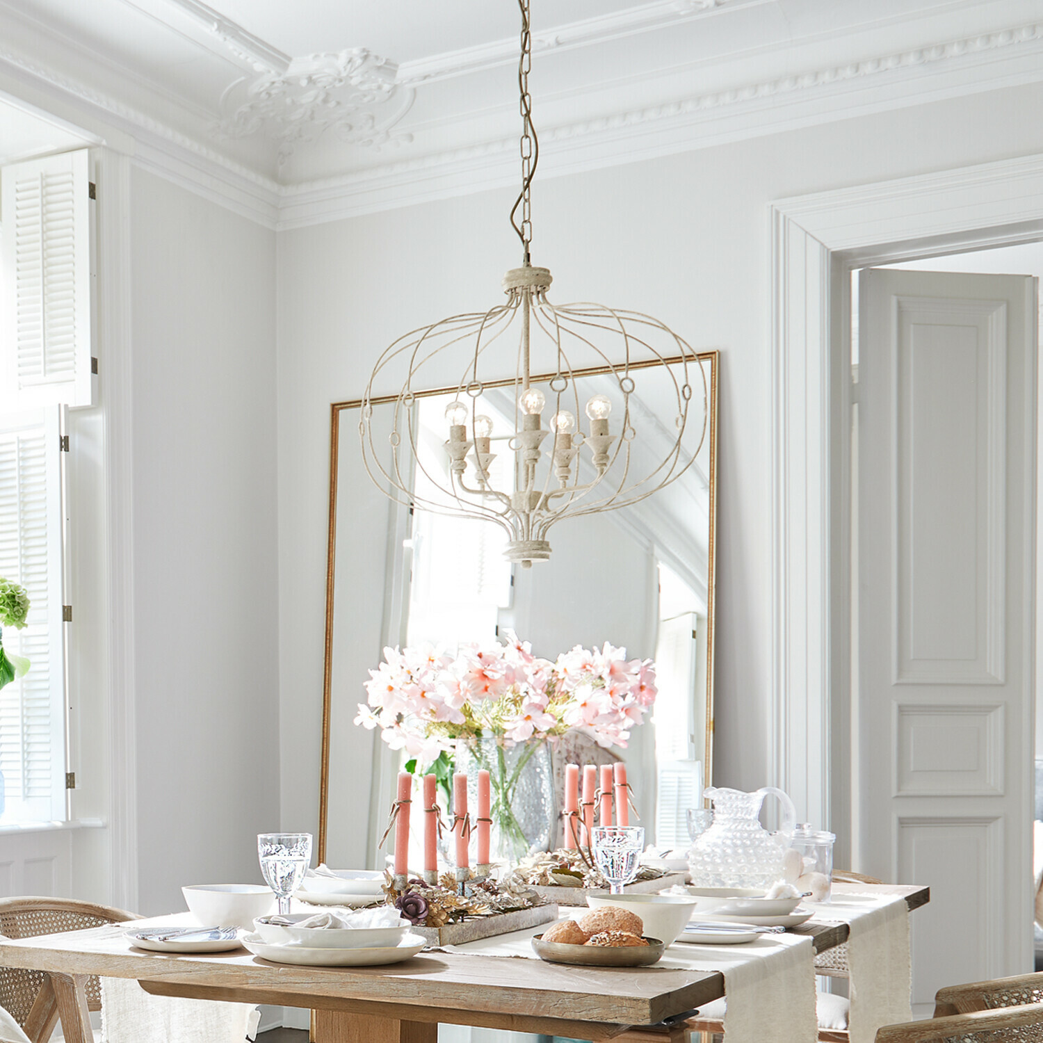 Heller Essbereich mit Holztisch, rosa Kerzen und vintage Metall-Kronleuchter über dem Tisch