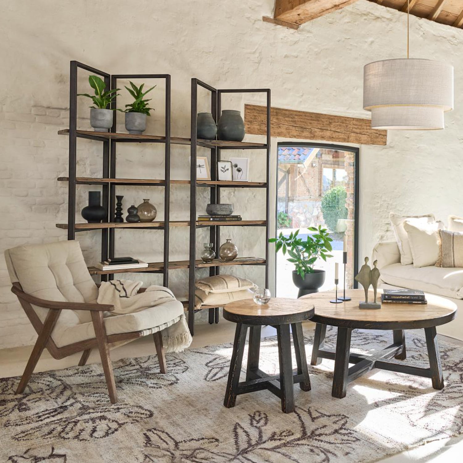 Gemütliches Wohnzimmer mit Holzsessel, Metall-Holz-Regal und runden Couchtischen auf gemustertem Teppich