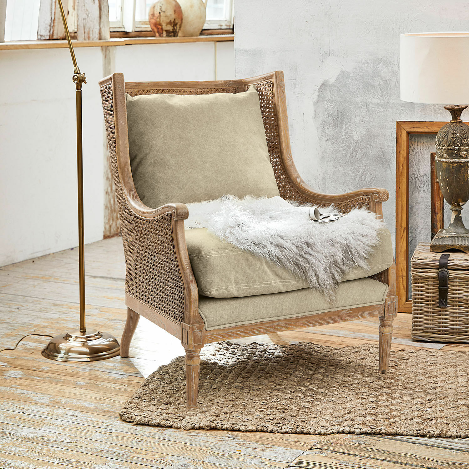 Sessel Greenbrier Sessel aus Holz und Rattan mit beigem Kissen und weißem Fellplaid auf Naturteppich im Raum