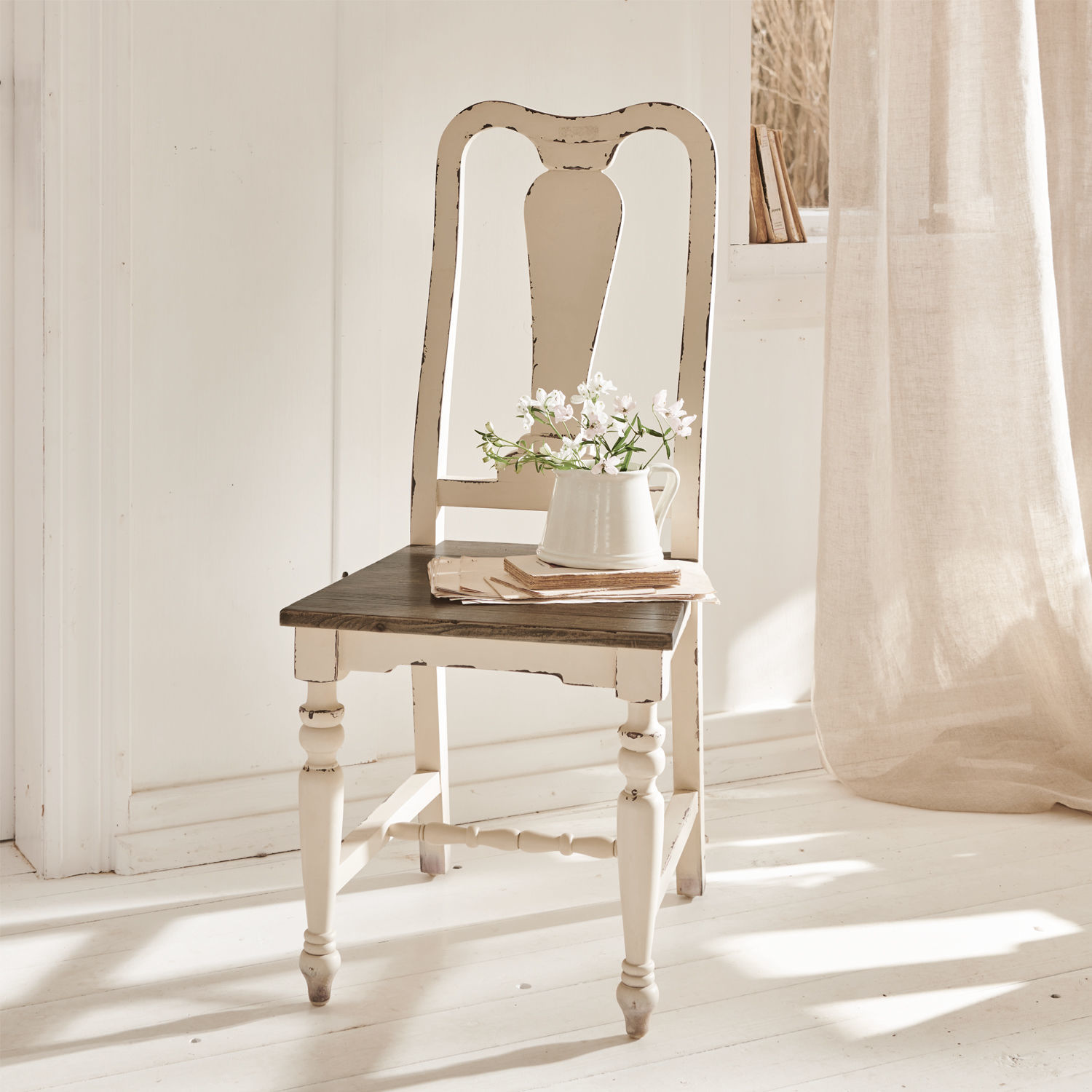 Stuhl Harry Weißes Holzstuhl im Vintage-Stil mit dunklem Sitz und Krug mit Blumen in hellem Raum