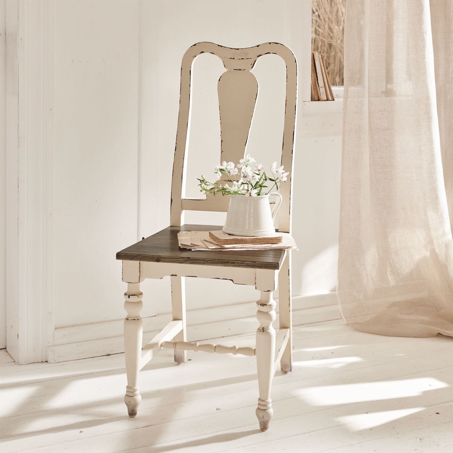 Stuhl Harry Weißes Holzstuhl im Vintage-Stil mit dunklem Sitz und Krug mit Blumen in hellem Raum