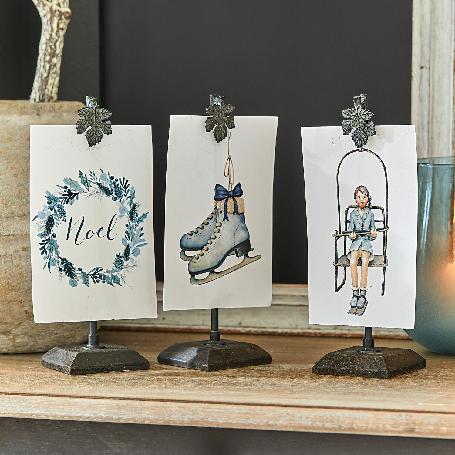 Drei Metallständer mit Klammern und winterlichen Karten in Blau- und Weißtönen auf Holzuntergrund