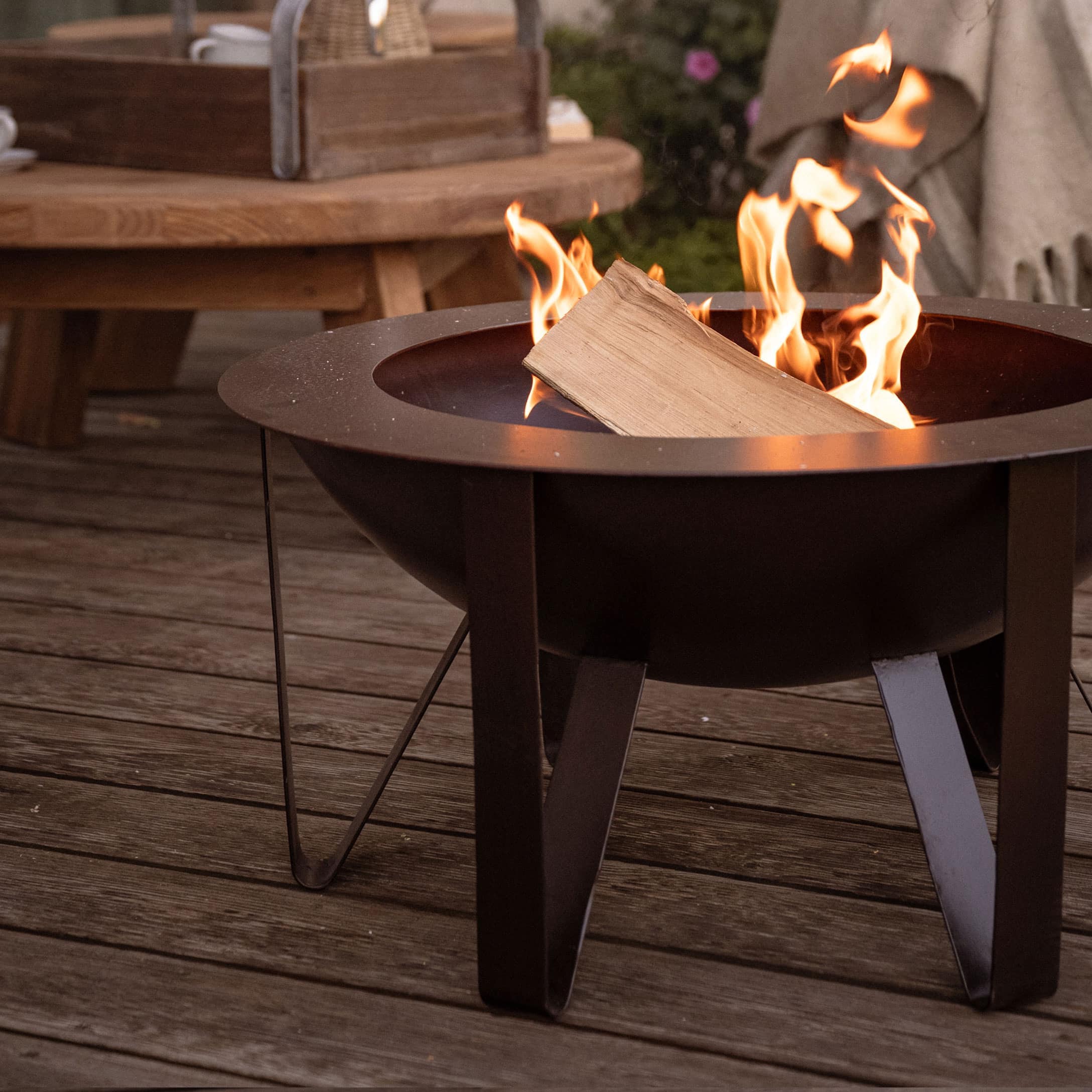 Schwarzes Metall-Feuerkorb mit brennendem Holz auf Holzterrasse für gemütliche Abende
